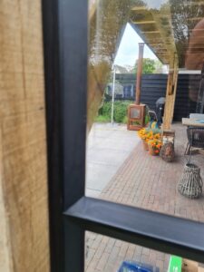 Wand van staal en glas met stopverf onder overkapping, By Siebendesign